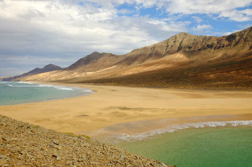 Playa de Cofete mit breitem Sandstrand, türkisfarbenem Meer und Bergkette im Hintergrund