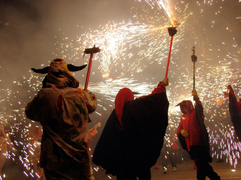Fuerteventura Menschen in traditionellen Kostümen mit Kapuzen und Masken schwenken Funken sprühende Feuerwerksstäbe bei Nacht. Umgeben von Rauch und Lichtblitzen während eines Festumzugs