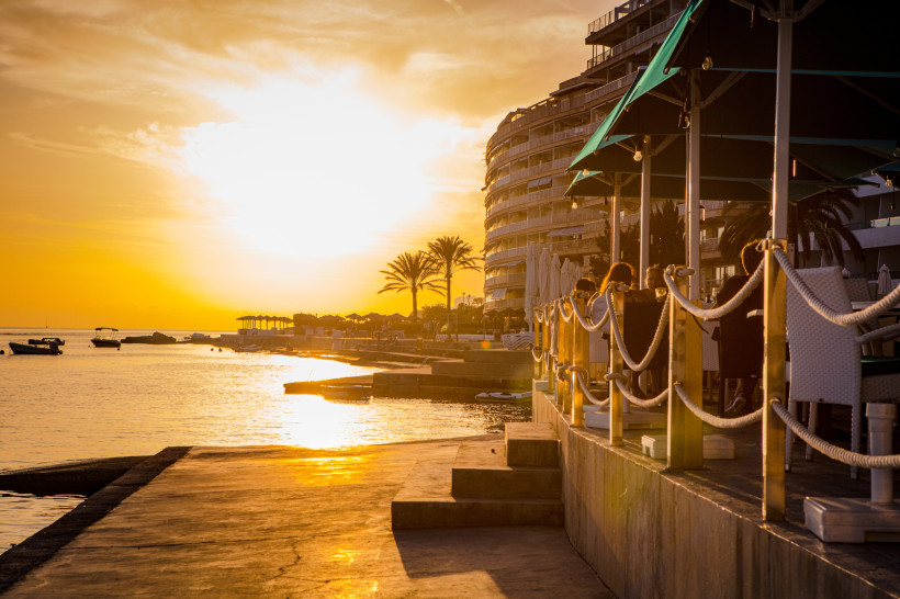 Sonnenuntergang an der Uferpromenade in Santa Ponsa mit Strand, Palmen und Restaurantterrasse am Wasser