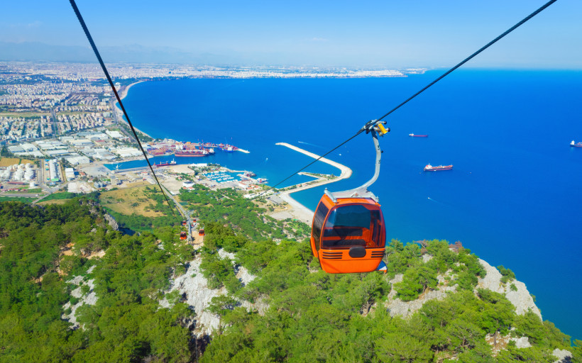 Tünektepe-Seilbahn Antalya – Panorama-Seilbahnfahrt mit Blick auf Mittelmeer Tünektepe-Seilbahn in Antalya mit roter Gondel über der Küste und Blick auf das tiefblaue Mittelmeer und den Hafen