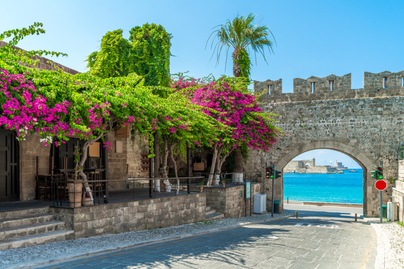 Historisches Stadttor in der Altstadt von Rhodos mit blühender Bougainvillea und Blick auf das türkisfarbene Meer