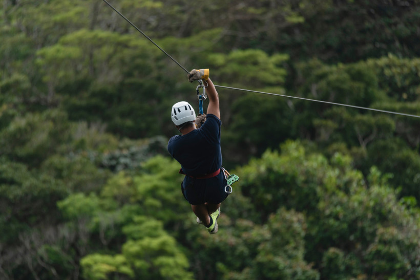 Costa Rica, Aktivurlaub  Person mit Helm beim Ziplining über einem tropischen Dschungel, Blick von hinten auf die Seilrutsche