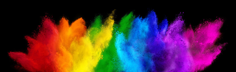 Explosion von buntem Farbpulver auf schwarzem Hintergrund. Die Farben verlaufen von links nach rechts in Regenbogenabfolge: Rot, Orange, Gelb, Grün, Blau, Violett und Pink. Die Pulverwolken wirken dynamisch und kraftvoll
