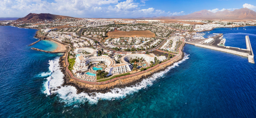 Playa Blanca auf Lanzarote – Luftaufnahme der Promenade, Hotels und der Marina Rubicón Luftaufnahme von Playa Blanca im Süden Lanzarotes mit türkisfarbenem Meer, Promenade, Hotels und der Marina Rubicón vor vulkanischer Landschaft.