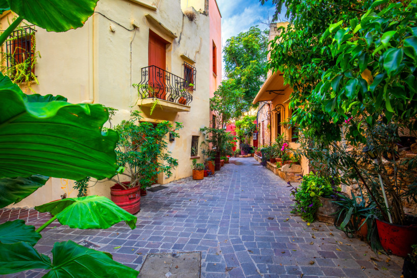 Gepflasterte Gasse in Chania mit pastellfarbenen Häusern, Balkonen und vielen Topfpflanzen