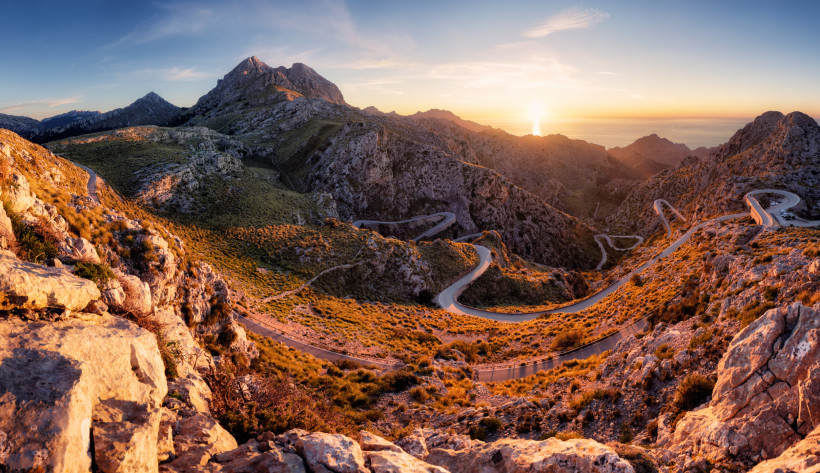 Serpentinenstraße in der Sierra de Tramontana bei Sonnenuntergang, Blick über felsige Berglandschaft bis zum Meer