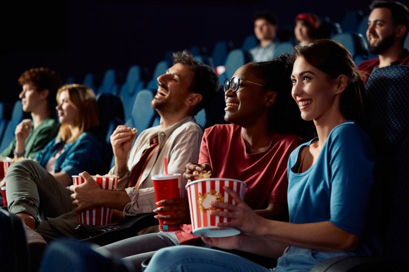 Ägypten - Hurghada Mehrere junge Menschen sitzen im Kino, lachen und genießen Popcorn und Getränke. Die Stimmung ist ausgelassen und fröhlich, die Sitze sind blau und der Raum leicht abgedunkelt.
