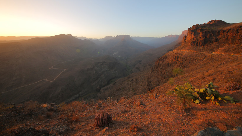 Sonnenuntergang über dem Fataga-Tal auf Gran Canaria mit roter Felslandschaft, kurviger Straße und Bergen im Hintergrund