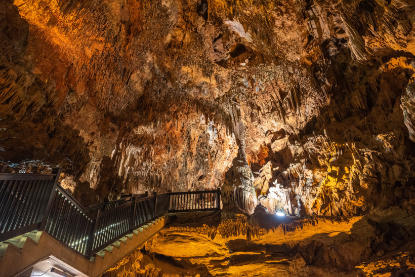 Beleuchteter Besucherweg in der Damlataş-Höhle in Alanya, mit sichtbaren Stalaktiten und Stalagmiten an der Decke und den Wänden der Höhle.