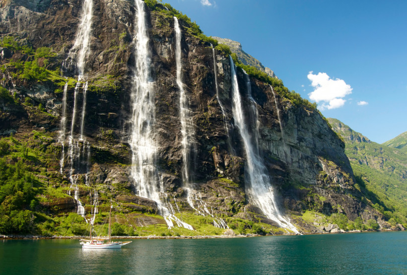 Wasserfälle an steiler Felswand in einem Fjord in Norwegen Mehrere Wasserfälle stürzen eine steile Felswand in einem norwegischen Fjord hinab; Segelboot auf dem Wasser