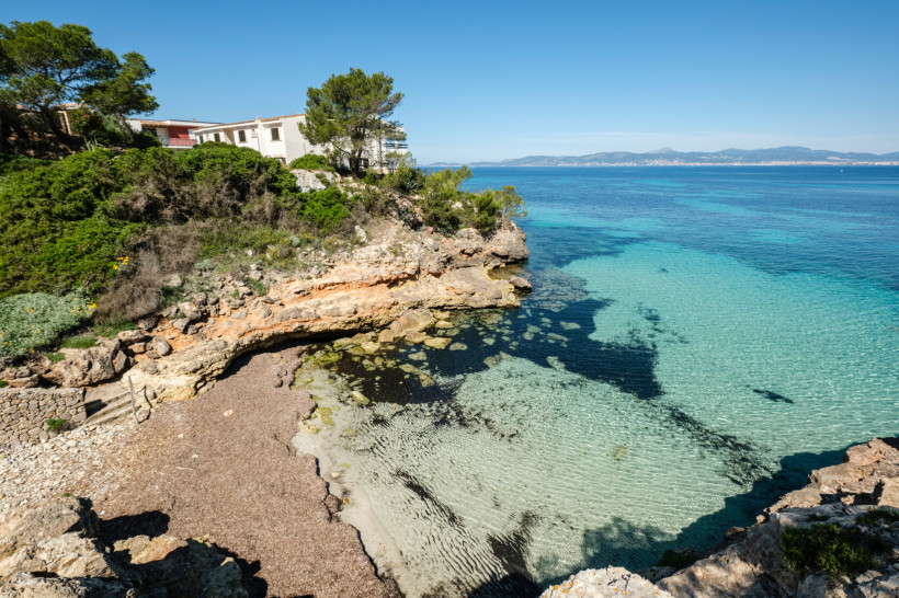 Felsige Küste mit kleiner Bucht, klarem türkisfarbenem Wasser und Häusern oberhalb der Klippen