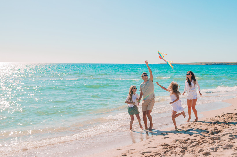 Fujairah, Familienferien  Familie spielt mit einem Drachen am sonnigen Strand, während die Wellen ans Ufer treffen.
