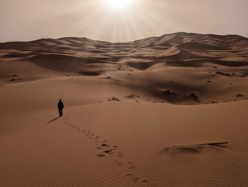 Erg Chebbi – Sanddünen in der Sahara bei Merzouga, Marokko Person wandert durch die goldenen Sanddünen des Erg Chebbi in der Sahara bei Merzouga, Marokko – spektakuläre Wüstenlandschaft bei Sonnenlicht.