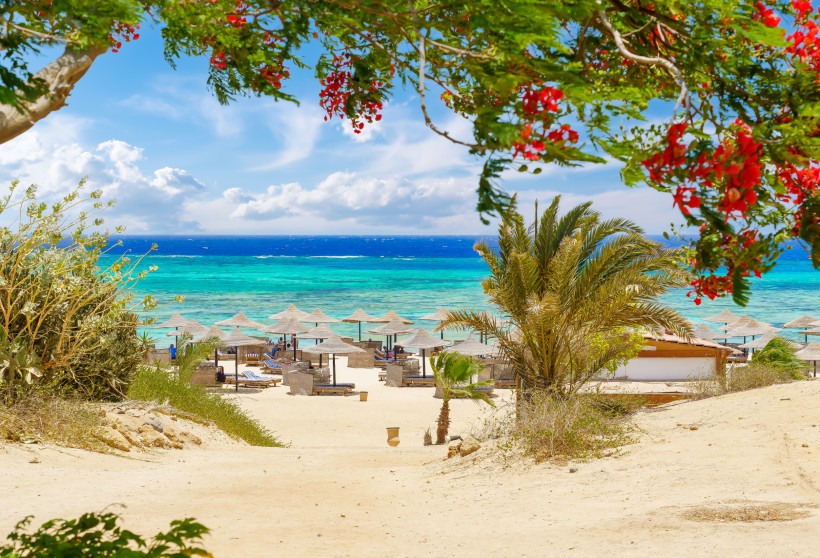 Sandweg zum Strand von Marsa Alam mit Sonnenschirmen und türkisfarbenem Meer