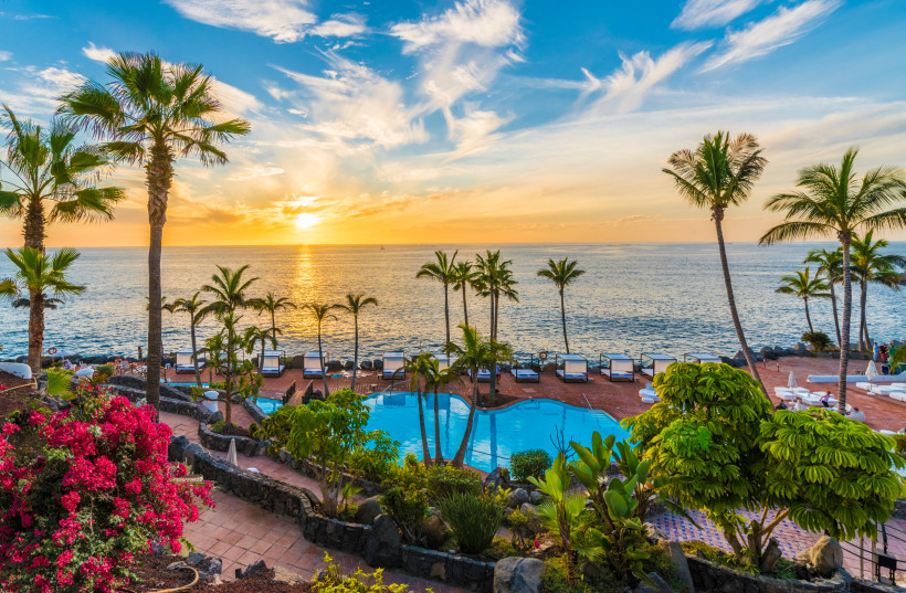 Sonnenuntergang über dem Atlantik in Adeje auf Teneriffa mit Palmen, Poolanlage und Liegen am Meer