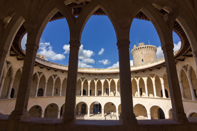 Innenhof des Castell de Bellver mit Arkadengängen und Blick auf den runden Wehrturm unter blauem Himmel