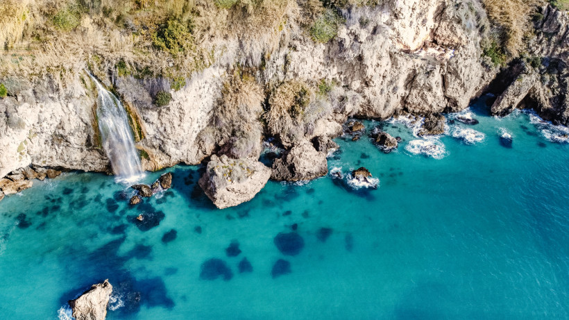 Wasserfall bei Nerja an einer Felsklippe, der ins türkisfarbene Meer stürzt