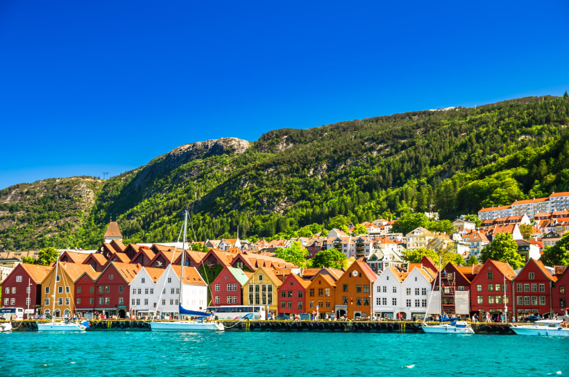 Bryggen, Bergen: farbige Häuserzeile am Hafen vor bewaldetem Berghang Bryggen in Bergen mit farbigen Hansehäusern am Hafen, Booten im Vordergrund und bewaldetem Berghang im Hintergrund