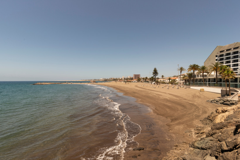 Sandstrand und Uferlinie in San Agustín auf Gran Canaria mit ruhigem Meer, Palmen und Hotelgebäuden