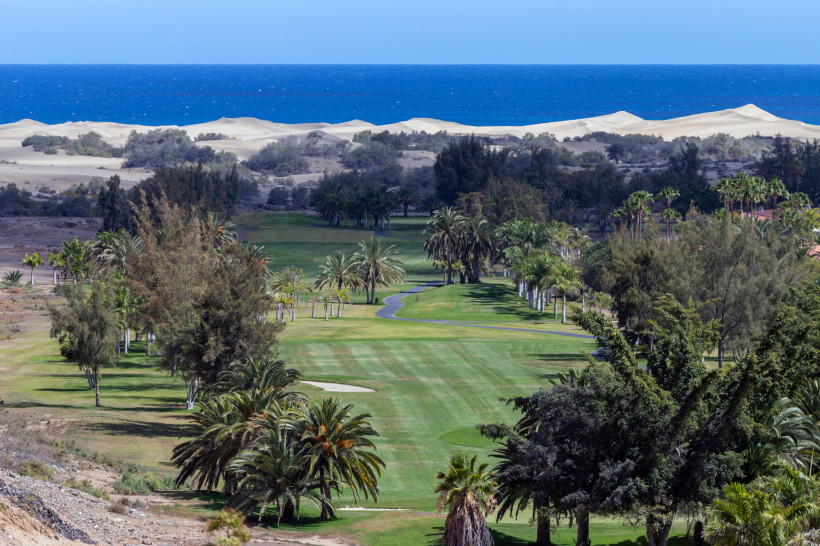 Blick über den Golfplatz Maspalomas mit Palmen, Fairway und Dünen am Meer im Hintergrund