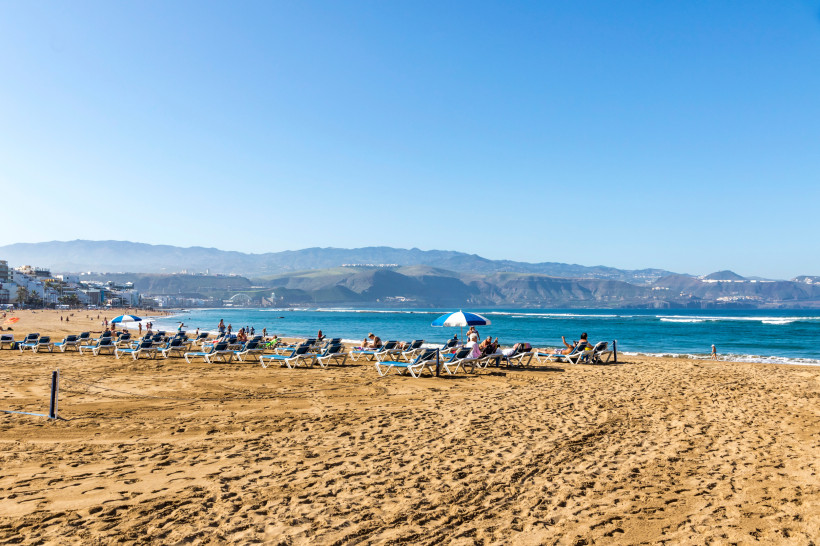Playa de Las Canteras mit Sandstrand, Liegestühlen und Sonnenschirmen am Meer, Berge im Hintergrund