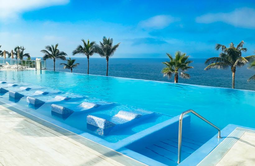 Infinity Pool mit Meerblick auf Gran Canaria – Entspannung mit Palmen und Atlantikkulisse Moderner Infinity Pool mit eingelassenen Liegen und Blick auf den Atlantik auf Gran Canaria. Palmen rahmen die Szenerie ein, der Himmel ist klarblau – ein Ort für Ruhe, Luxus und Entspannung am Meer.