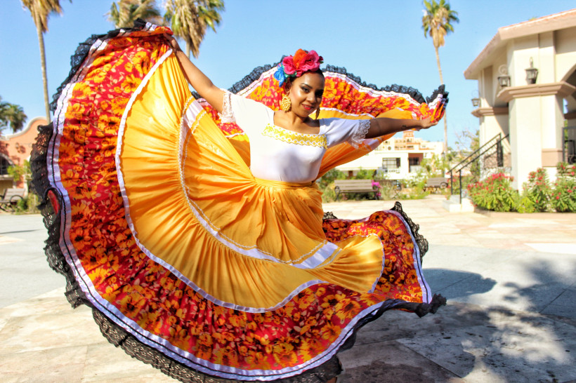 Carnaval in Mexiko Mexikanische Tänzerin in einem bunten, traditionellen Kleid mit gelben und roten Farbtönen führt einen folkloristischen Tanz auf, während sie das Kleid schwungvoll bewegt