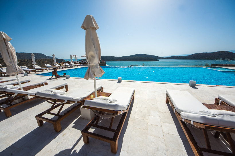 Poolterrasse eines Luxushotels in Elounda mit Sonnenliegen und Blick auf die Bucht