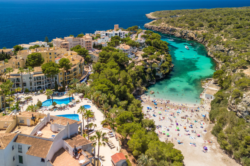Luftaufnahme der Bucht Cala Pi mit türkisfarbenem Wasser, Sandstrand, Felsküste und Häusern am Ufer