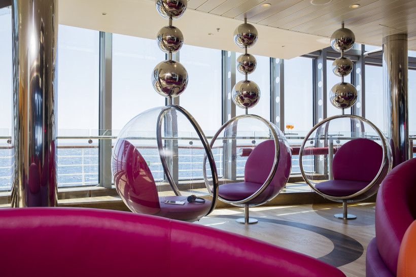 Lounge im Theatrium der AIDAprima mit runden Sitzkapseln vor großen Panoramafenstern und Meerblick