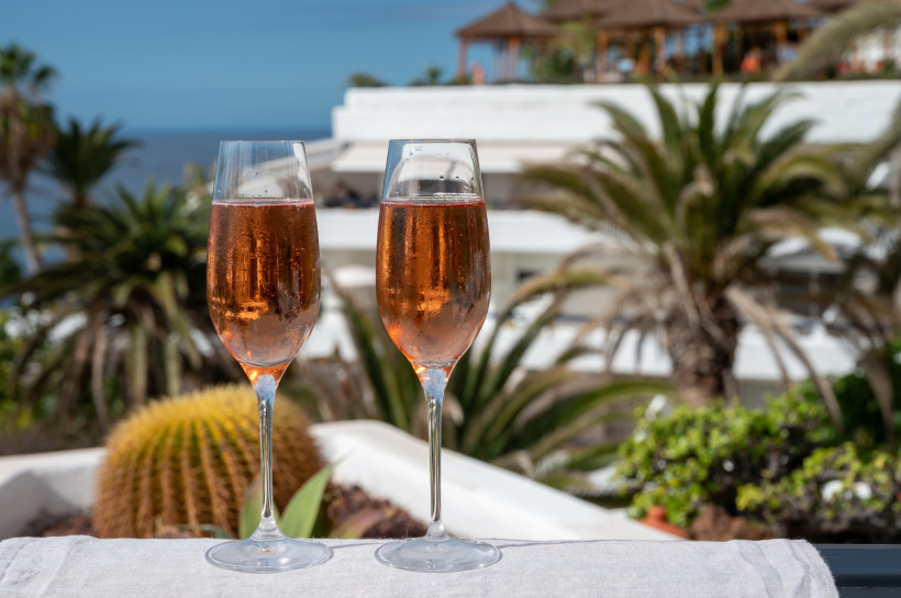 Luxusurlaub auf Fuerteventura – stilvoll entspannen mit Meerblick und Champagner Zwei Gläser Rosé-Sekt auf einer Terrasse mit Palmen und Meerblick – Symbol für stilvollen Luxusurlaub auf Fuerteventura