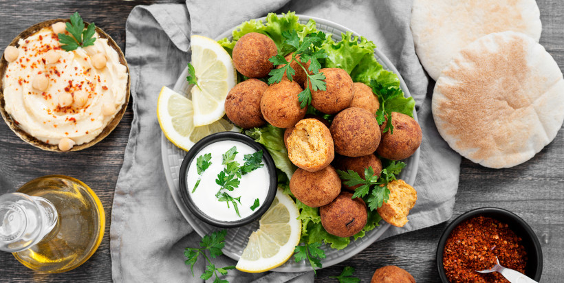 Ägypten Ein Teller mit knusprigen Falafelbällchen auf Salat, serviert mit Zitronenscheiben, Joghurt-Dip, Fladenbrot und Hummus. Dazu Gewürze und eine Flasche Olivenöl auf einem dunklen Holztisch