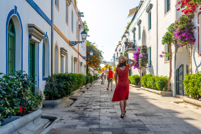 Spaziergang durch Puerto de Mogán Eine Frau in rotem Kleid schlendert durch die blumengeschmückten Gassen von Puerto de Mogán auf Gran Canaria. Die weißen Häuser mit bunten Fensterrahmen verleihen dem Ort ein mediterranes Flair.