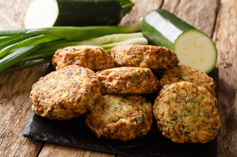 Kolokithokeftedes, griechische Zucchinipuffer, auf einer Schieferplatte mit Zucchini und Frühlingszwiebeln