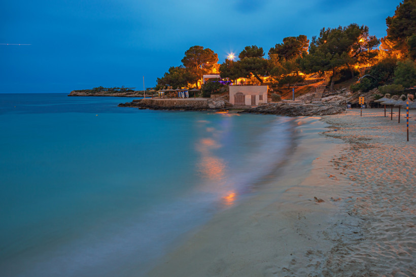 Bucht Cala Comtesa bei Illetas in der Abenddämmerung mit Sandstrand, ruhigem Meer und beleuchtetem Uferbereich