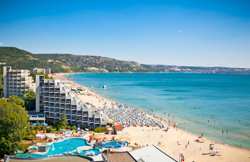 Bulgarien Blick auf ein belebtes Strandresort mit modernen Hotels an einem langen Sandstrand. Viele Sonnenschirme und Badende verteilen sich am türkisfarbenen Meer. Im Hintergrund grüne Hügel