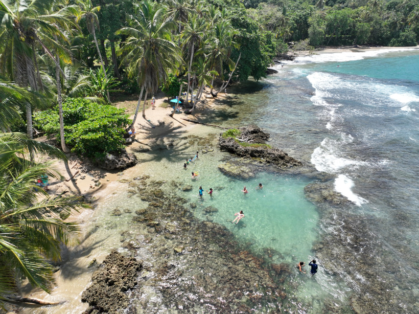 Costa Rica, Sommer Menschen baden in einem natürlichen Pool zwischen Felsen an einem tropischen Strand mit Palmen und türkisblauem Meer