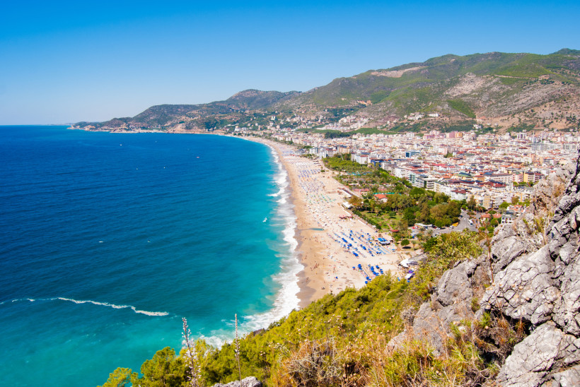 Dieses beeindruckende Foto zeigt den berühmten Kleopatra-Strand in Alanya, der sich entlang der türkischen Riviera erstreckt. Vom Felsen aus bietet sich ein weiter Blick auf das glasklare, tiefblaue Mittelmeer, das sanft an den kilometerlangen Sandstrand 