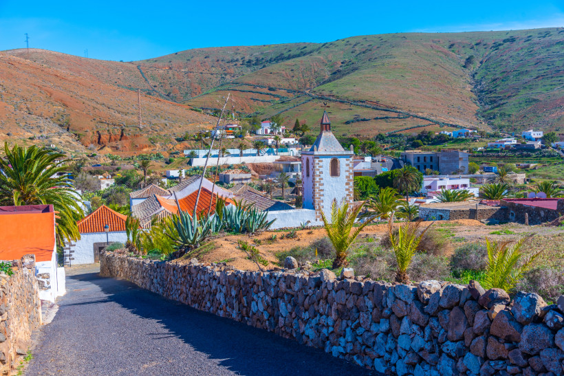 Betancuria Fuerteventura – Historisches Dorf inmitten grüner Berglandschaft Blick auf das historische Dorf Betancuria auf Fuerteventura mit weißem Kirchturm, traditionellen Häusern und umgebender grüner Berglandschaft.