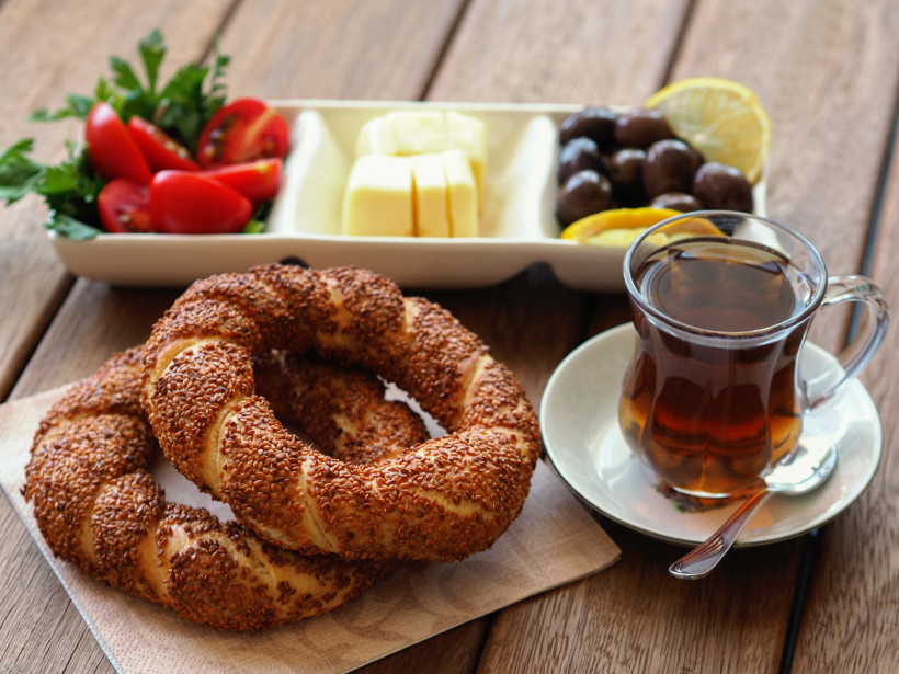 Türkisches Frühstück – Simit, Tee und mediterrane Spezialitäten Frisches Simit mit Sesam, türkischer Schwarztee im Glas, Oliven, Käse und Tomaten auf Holztisch – klassisches türkisches Frühstück und Teil der Esskultur in Antalya