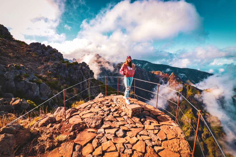 Frau auf dem Gipfel des Pico do Arieiro auf Madeira mit Blick auf die Berge und Wolkenlandschaft im Sonnenlicht