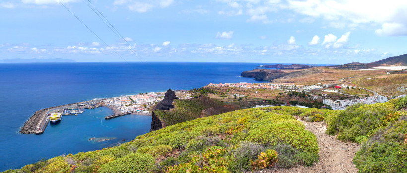 Panoramablick auf den Hafen von Puerto de las Nieves auf Gran Canaria mit Fähre, kleinen weißen Häusern und Küstenlandschaft, die ins blaue Meer übergeht.
