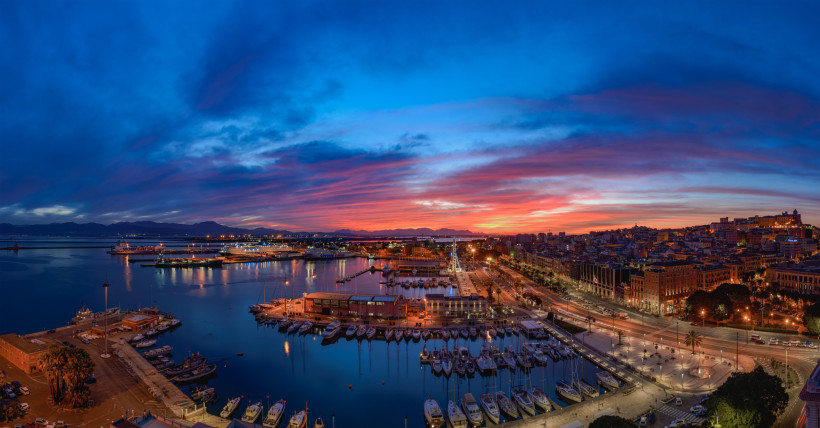 Panoramablick auf den Hafen von Cagliari bei Sonnenuntergang mit buntem Himmel, Lichtern der Stadt und Yachten im Mittelmeer – Hauptstadt Sardinien