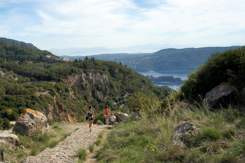 Wandern mit Aussicht: Eine Gruppe von Wanderern folgt einem schmalen Pfad durch Korfus hügelige Landschaft. Üppige Vegetation, steile Hänge und weite Ausblicke auf das Ionische Meer machen diese Route zu einem Naturerlebnis der besonderen Art – ideal für 