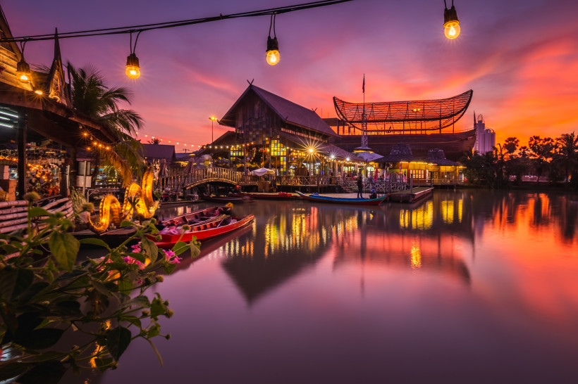 Romantische Abendstimmung am Floating Market in Thailand mit beleuchteten Booten Beleuchteter schwimmender Markt in Thailand bei Sonnenuntergang mit traditioneller Architektur, reflektierendem Wasser und dekorierten Booten