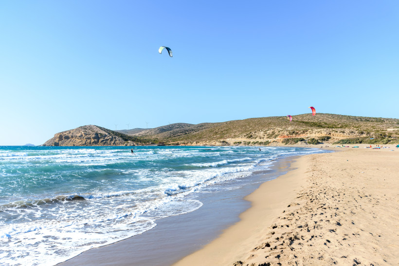 Langer Sandstrand auf Rhodos mit Wellen, Kitesurfern und türkisblauem Meer vor hügeliger Landschaft