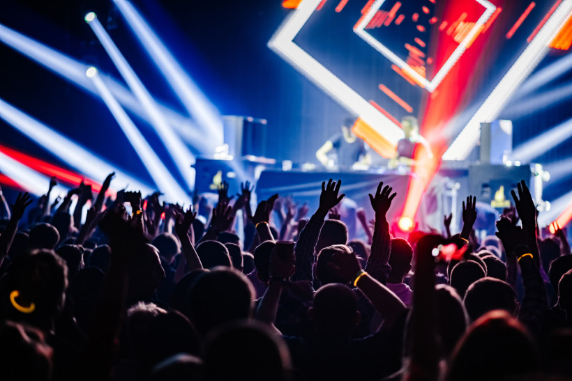 Publikum mit erhobenen Händen vor DJ-Pult in einem Nachtclub mit Lichtshow