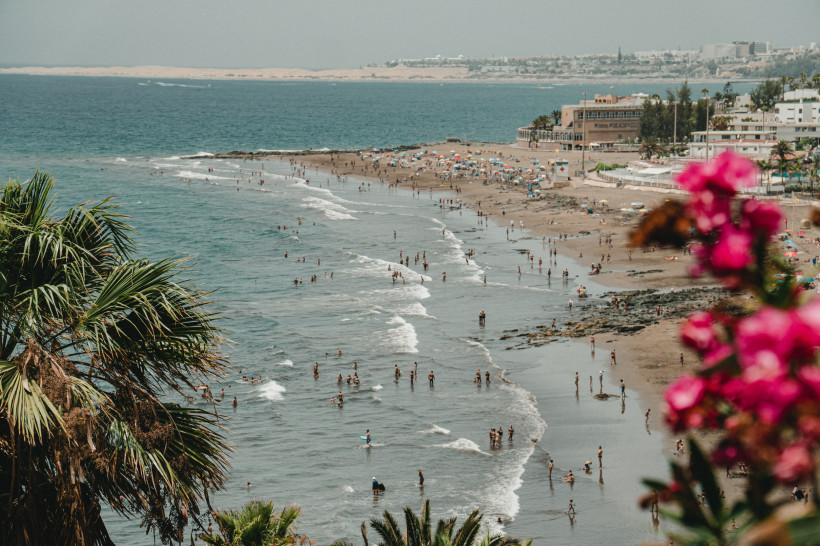 Blick auf die Playa de San Agustín mit Küstenlinie, Badenden im Meer und Gebäuden im Hintergrund
