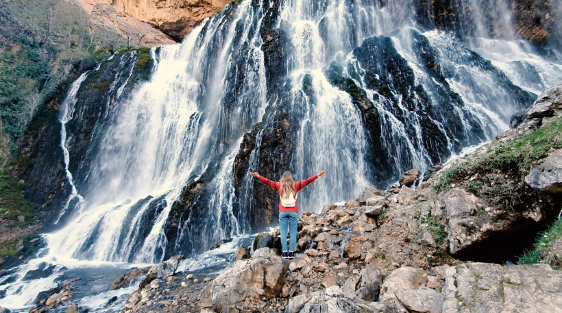 Winter in Belek: Naturerlebnisse Frau steht vor einem großen Wasserfall im Naturpark der Region Antalya – idealer Winterausflug während eines Urlaubs in Belek.