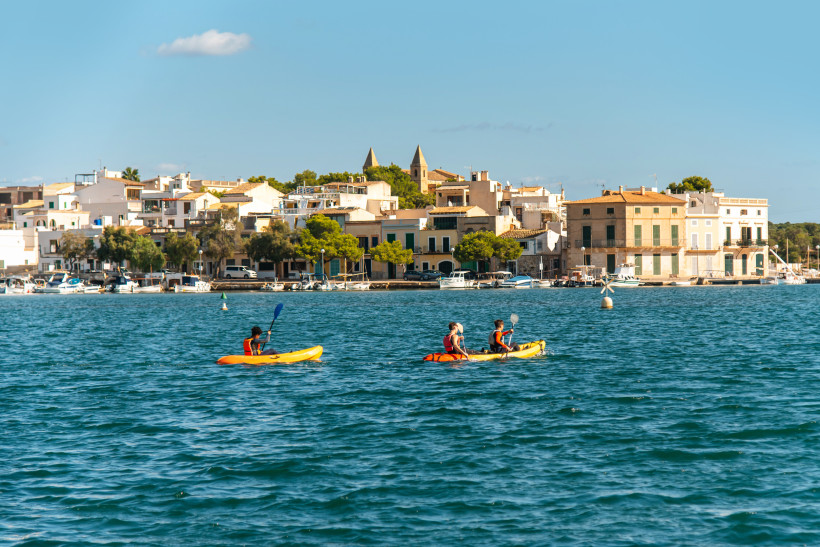 Kajakfahrer im Hafenbecken von Portocolom vor der Uferbebauung